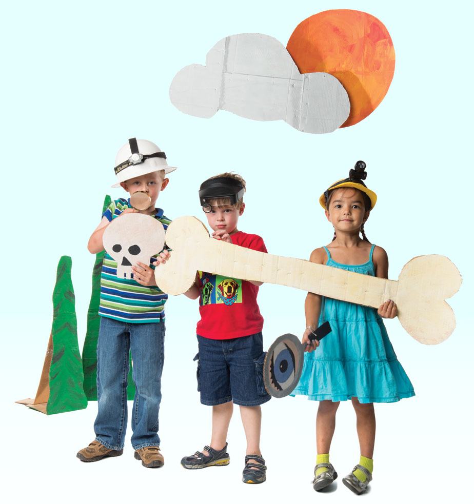 Photo of three children playing with cut-outs of skull, bones, and magnifying glass