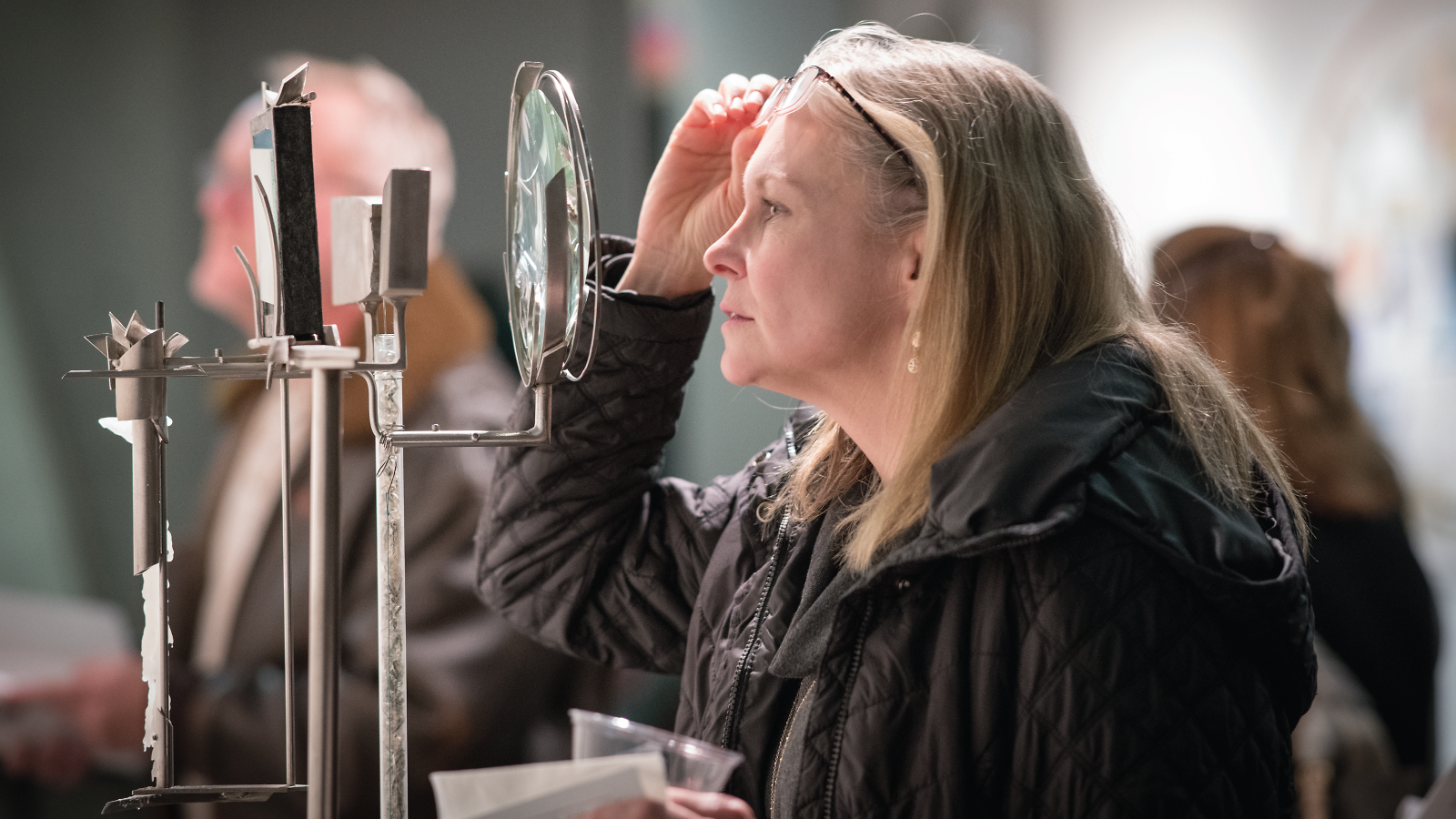 Photo at the artist’s reception for Jenkins’ show, a visitor peers through the magnifying glass of a sculpture