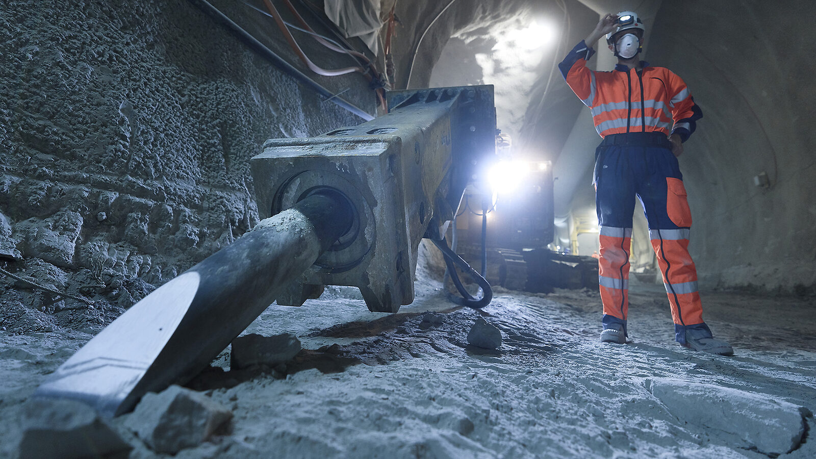 Photographer Samuel Hertzog, in an orange construction-site uniform, stands among heavy equipment in the tunnel