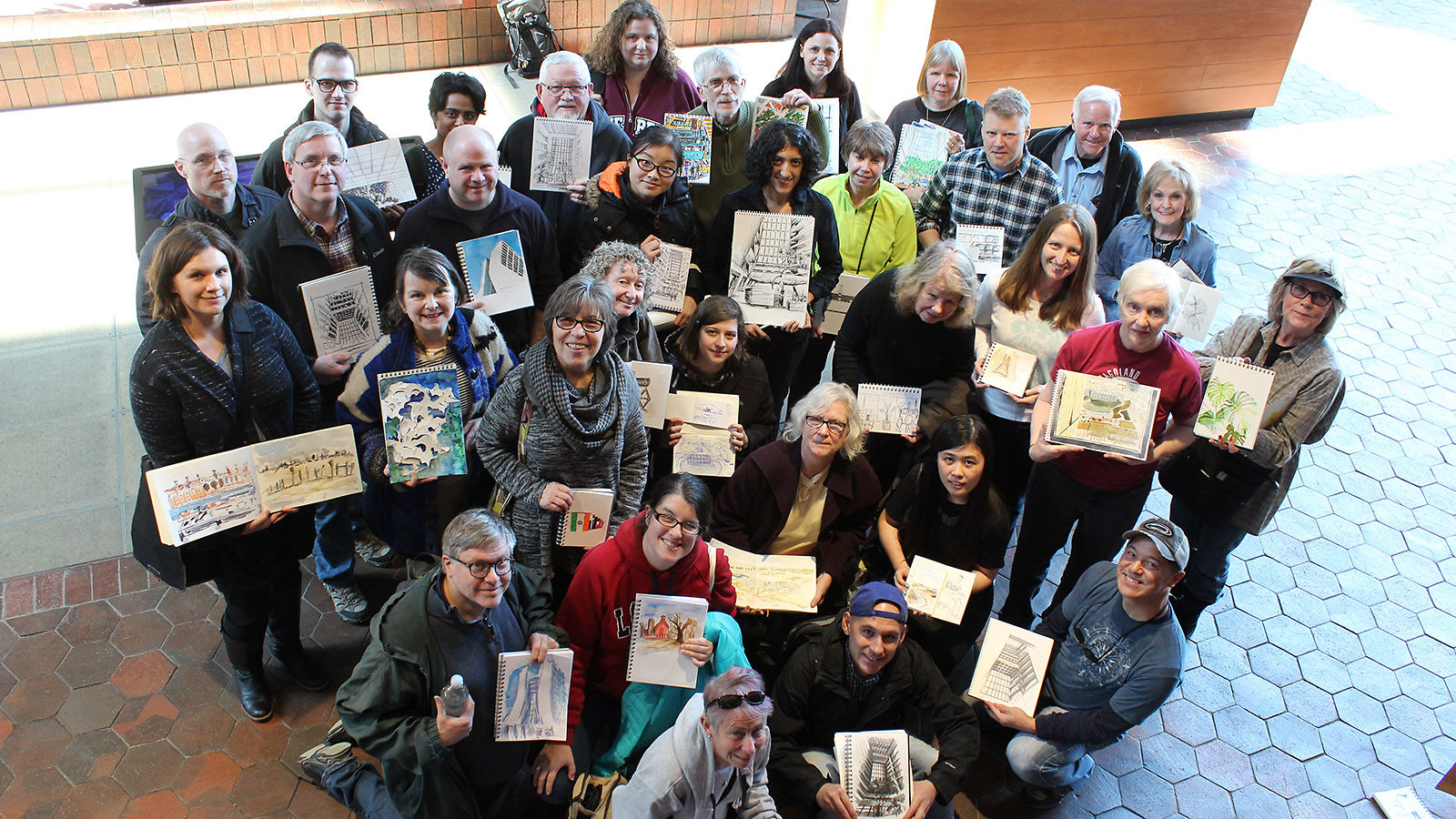 Group of about 30 people looks up at the camera holding their sketches