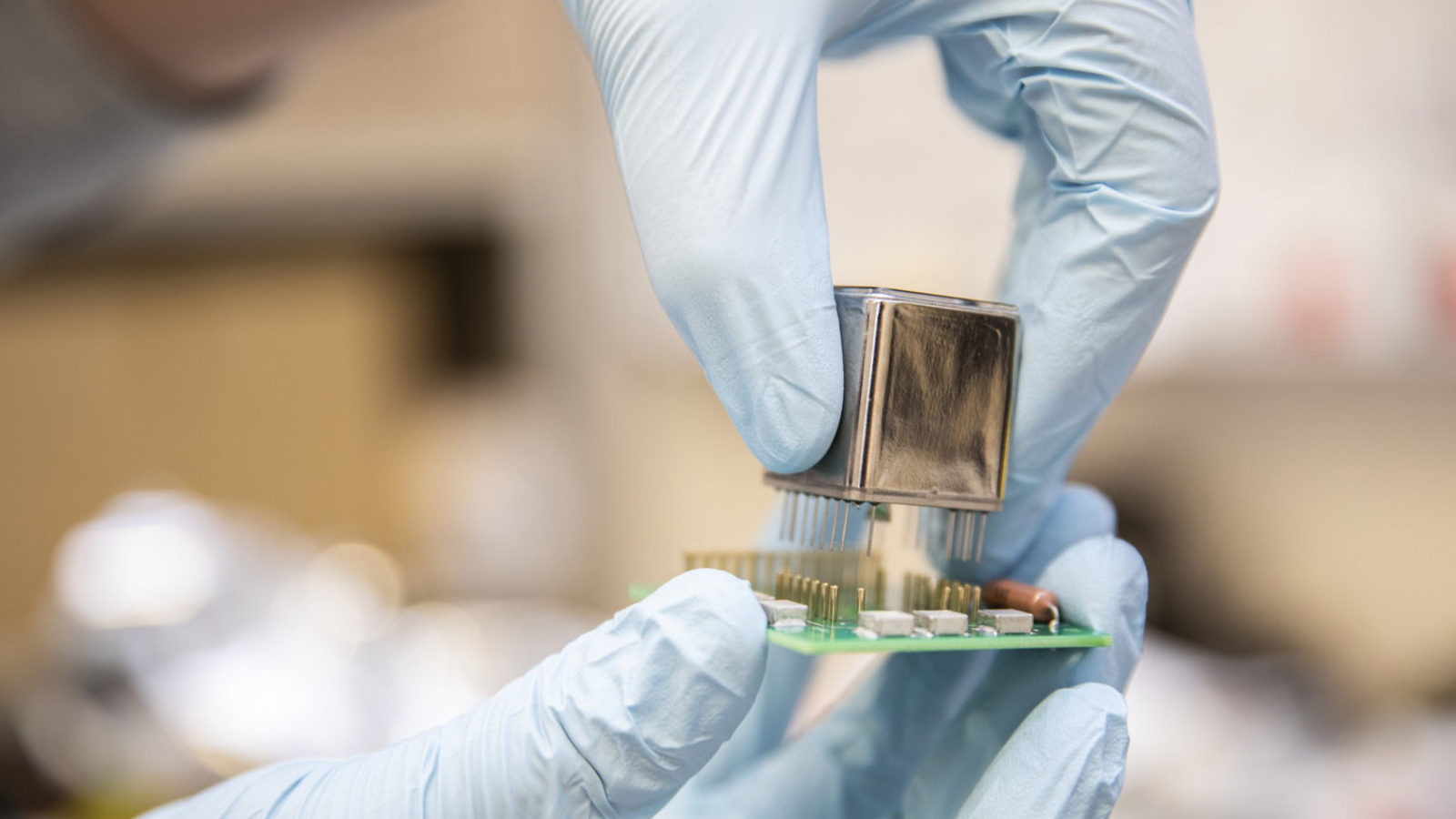 Photograph of hands in light blue rubber gloves holding detector components