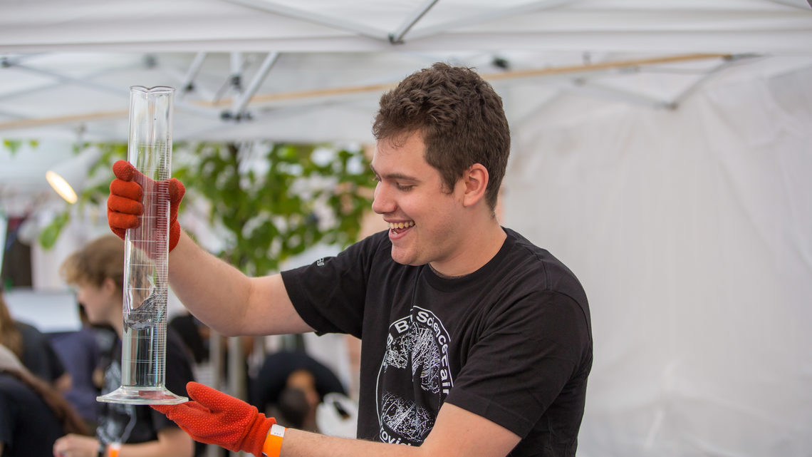 A volunteer enthusiastically demonstrates an experiment with a a graduated cylinder 