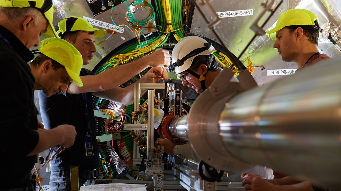Five people in protective hats work next to the CMS detector.