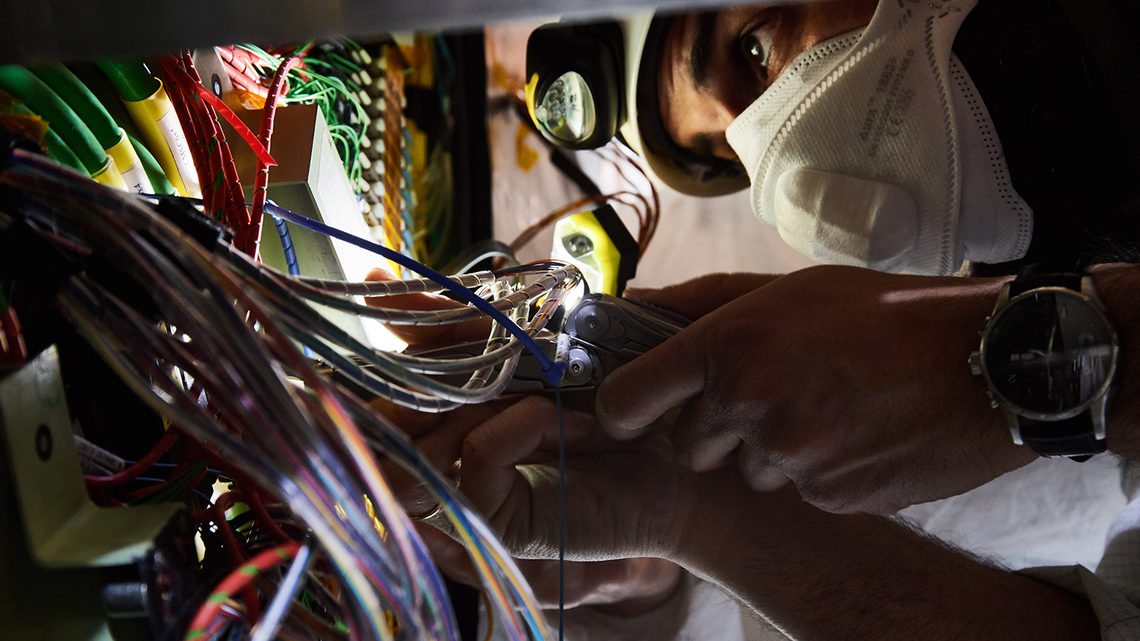 Close-up of a person wearing a cleanroom mask and a helmet with a light next to colorful cables.