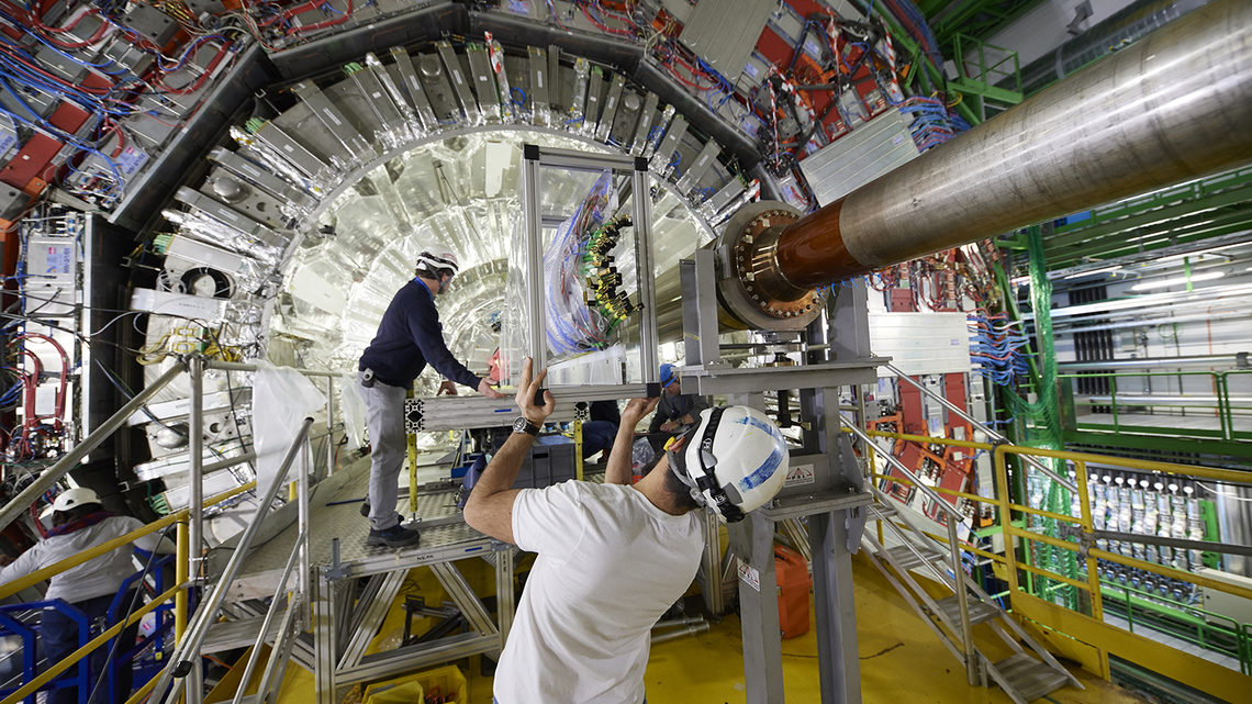 People in hard hats insert new parts into the CMS detector.