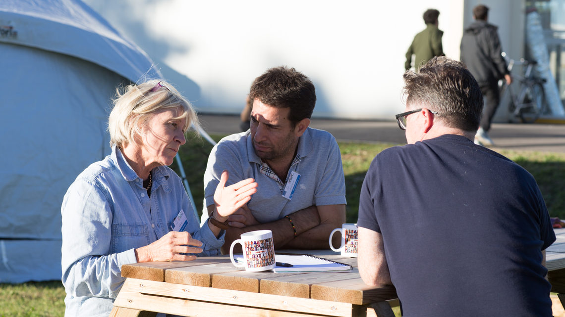 A woman and two men sitting at a picnic table talking 