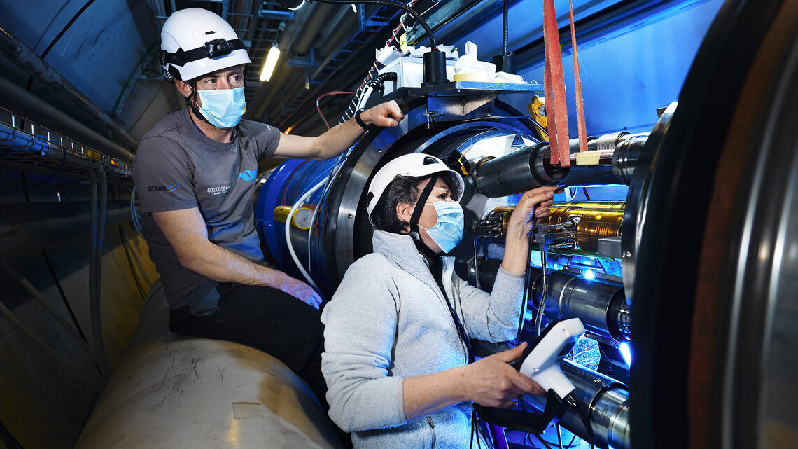 Photo of two people in surgical masks and hard hats working on the LHC tunnel