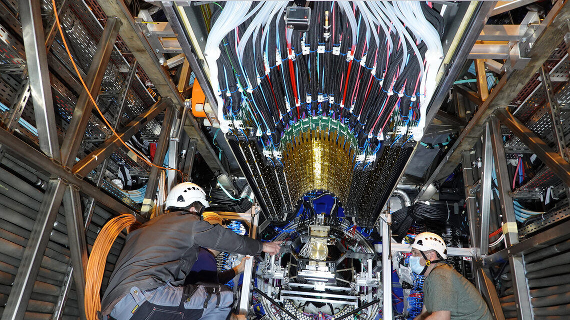 Photo of three people in hard hats working on a detector component