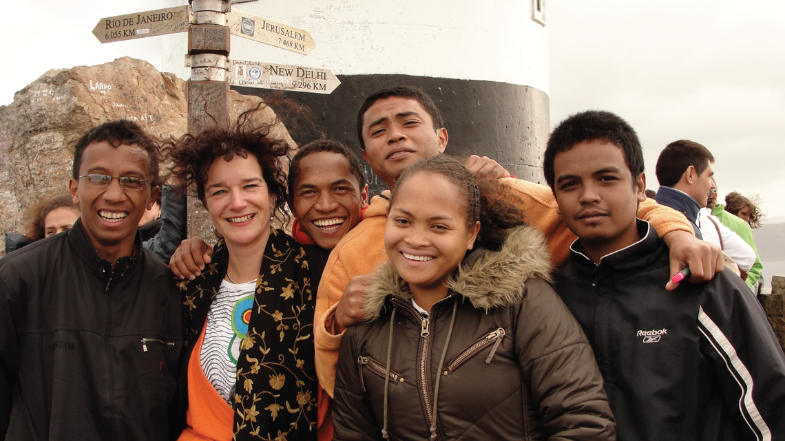 Group photo of African students wearing coats and standing in front of a sign indicating the distance to different cities