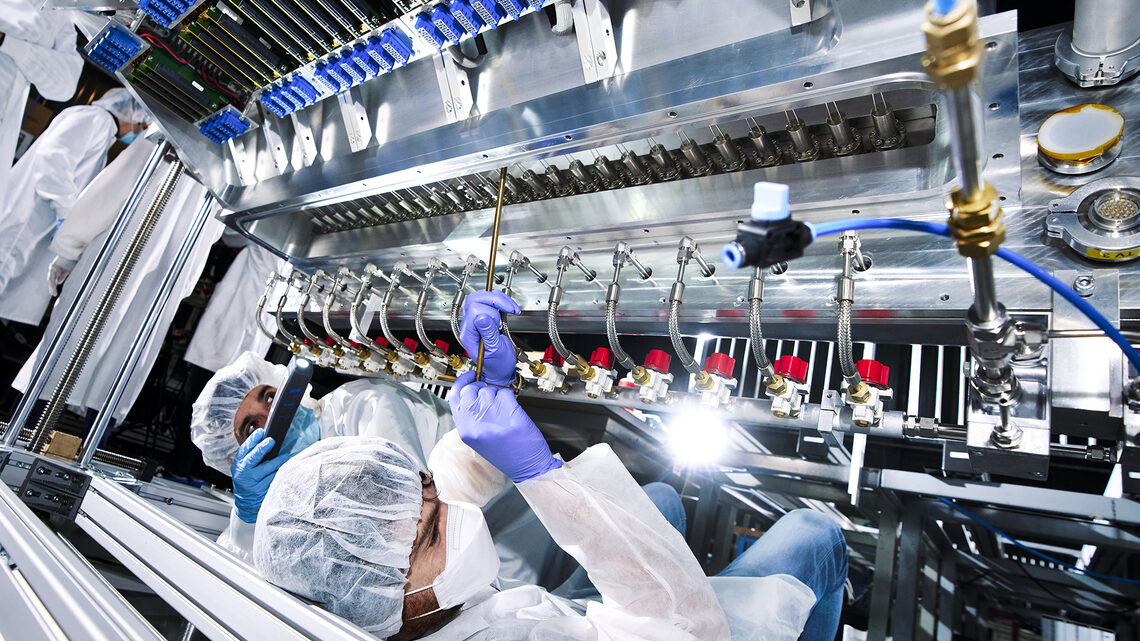 Photo of two people in clean-room garb working on a detector component