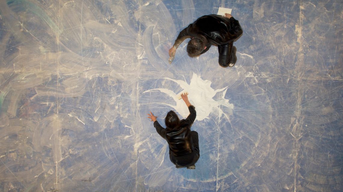 Overhead photograph of the artists sweeping the sand into a pile in the center