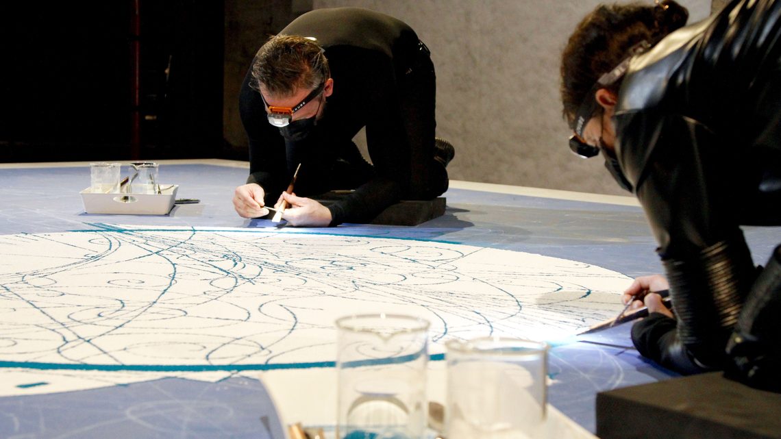 Side view photograph of the artists working on the sand mandala