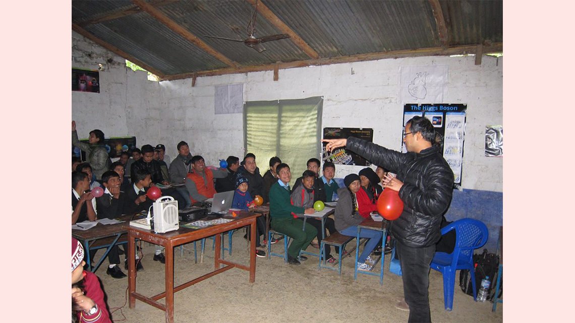 Photo of a person with a balloon standing in front of a classroom full of people, some of whom also have balloons