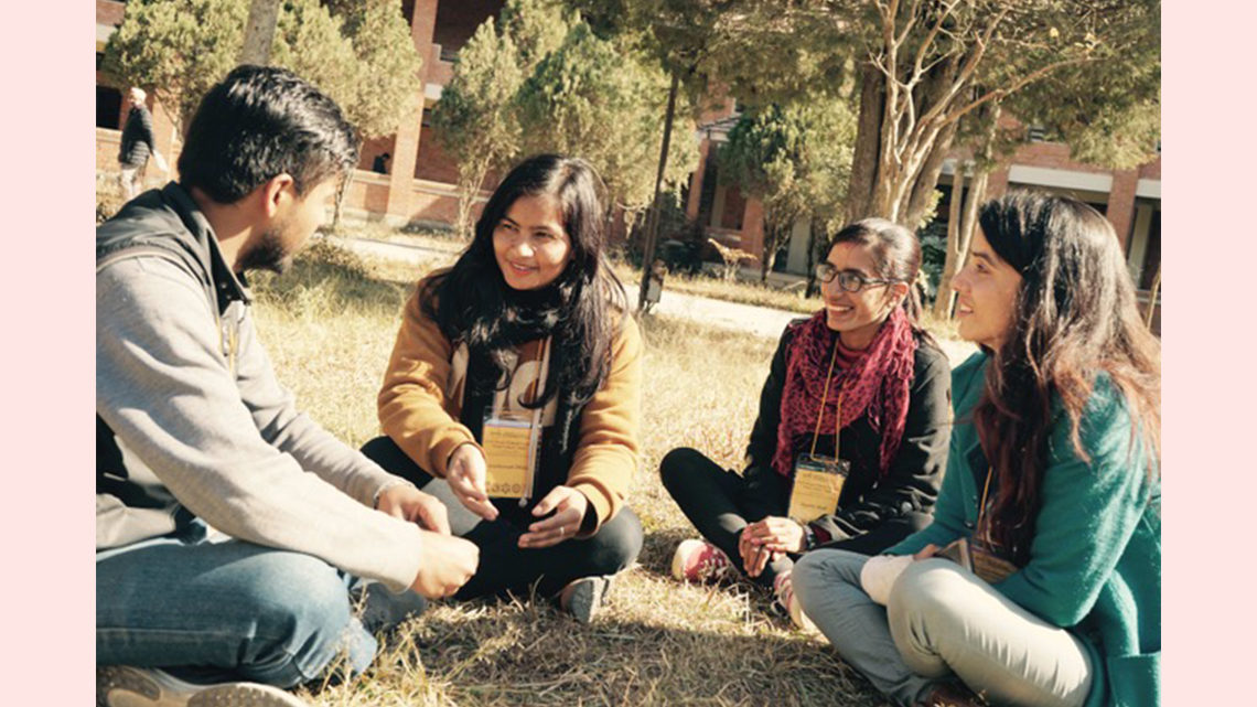 Photo of students sitting cross-legged on the ground outside with an instructor