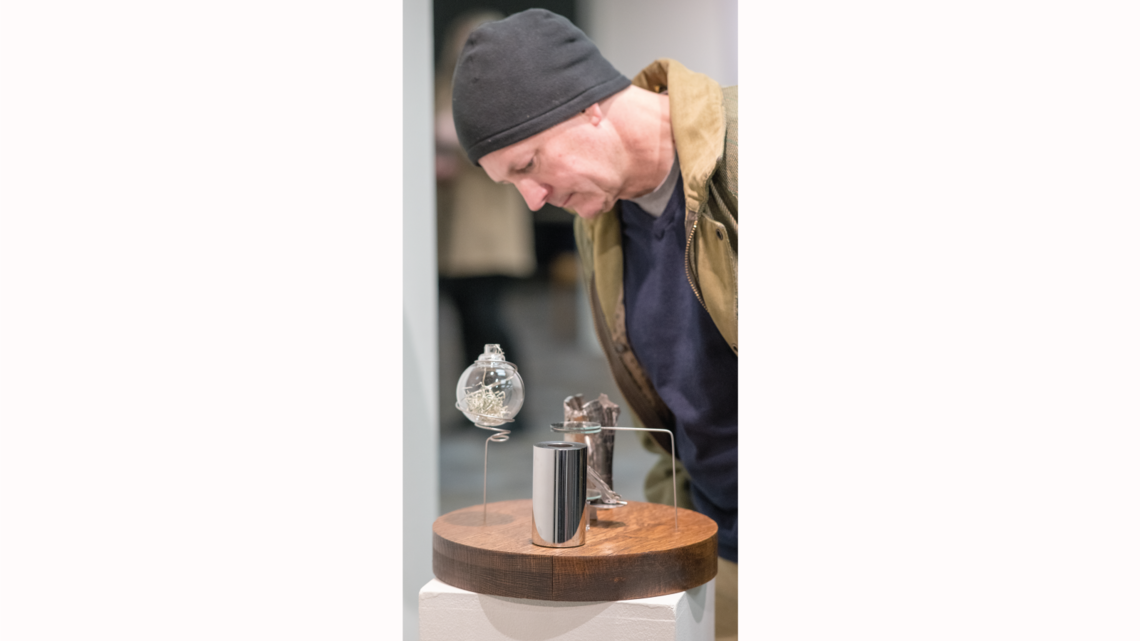 Photo of a visitor closely examines Beauty & Boredom at the artist’s reception of the gallery opening