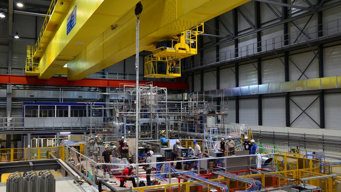 Photograph of people in hard hats examining the 25-foot thermometer, upright and attached to a crane