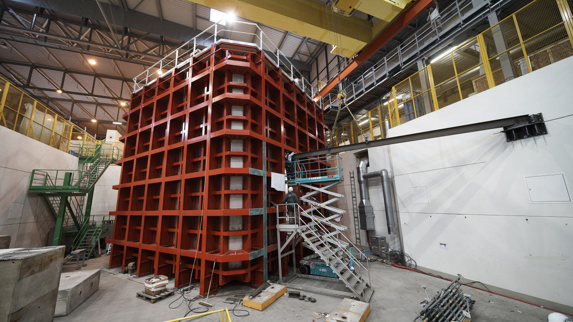 Photo of a person on a scissor lift standing next to the ProtoDUNE, red cube