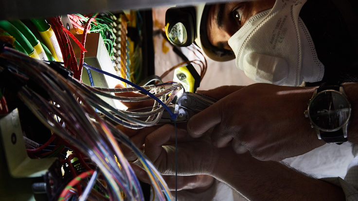 Close-up of a person wearing a cleanroom mask and a helmet with a light next to colorful cables.