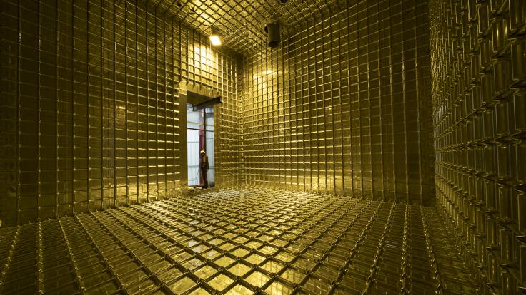 A figure is silhouetted in the opening of a gold-colored room.