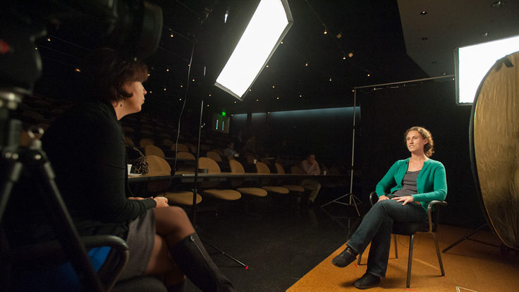 Photo of woman interviewing another woman in an auditorium, on stage