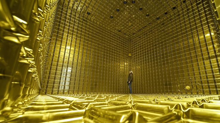 Photo of a person standing inside the ProtoDUNE detector, the walls, floor, and ceiling are all yellow