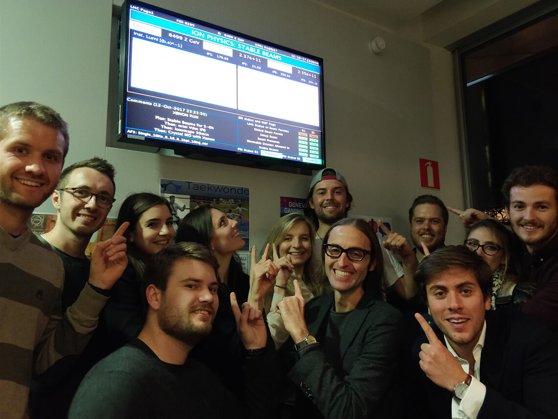A crowd of people point at a screen indicating that the xenon-xenon run has begun